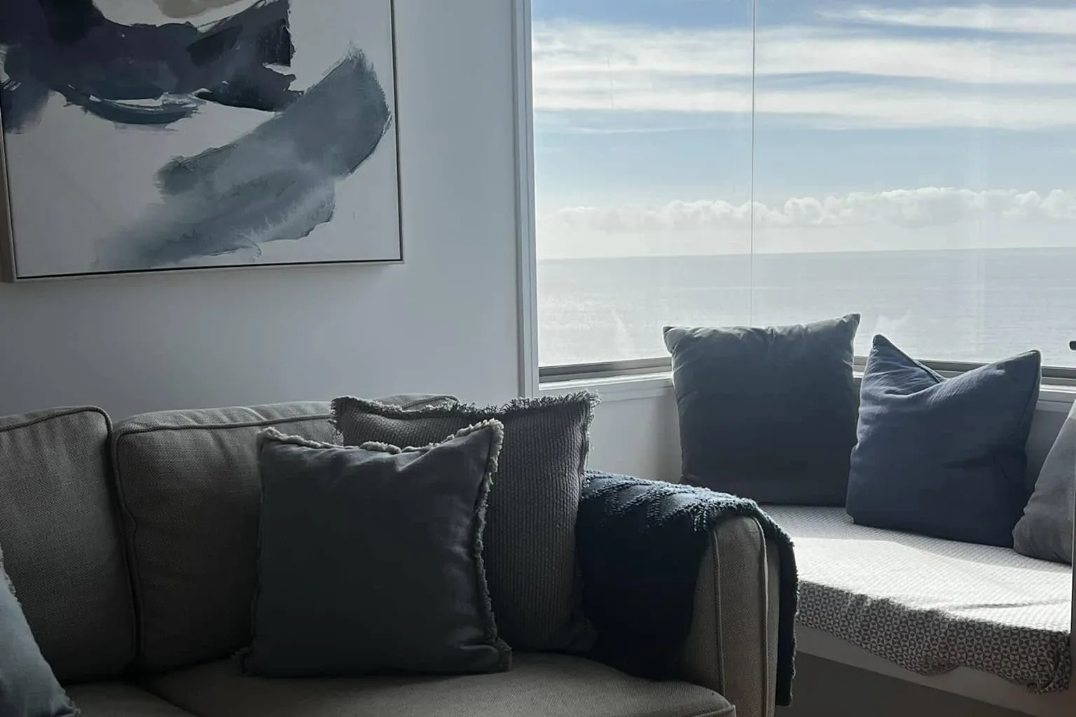 A grey sofa by a window with a seascape print above it