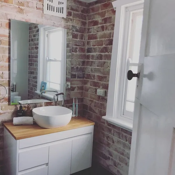 A bathroom with a brick wall, a timber vanity and a white basin, cleaned for guests