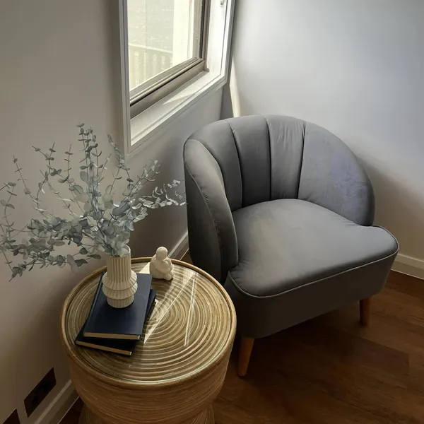 A grey armchair by the window with a cane side table