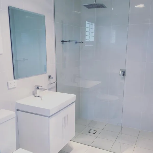 A white tiled bathroom with a glass shower screen
