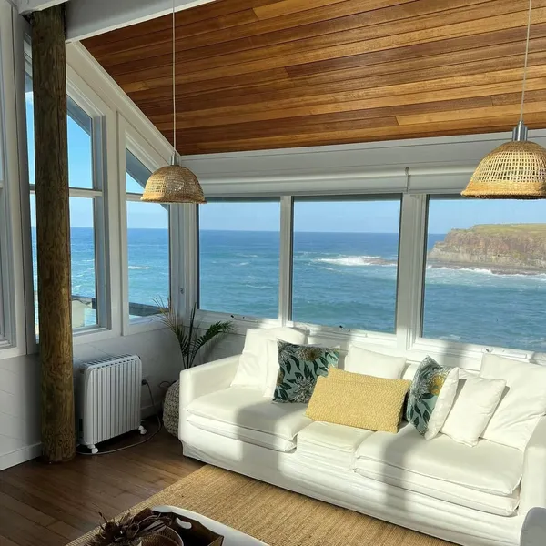 A white lounge with a timber ceiling and the sea through the windows