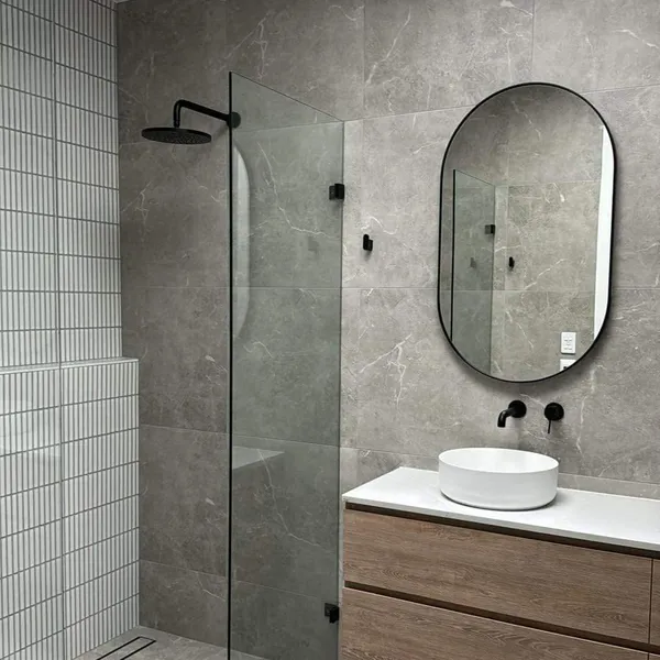 A grey-tiled ensuite with a clean glass shower screen