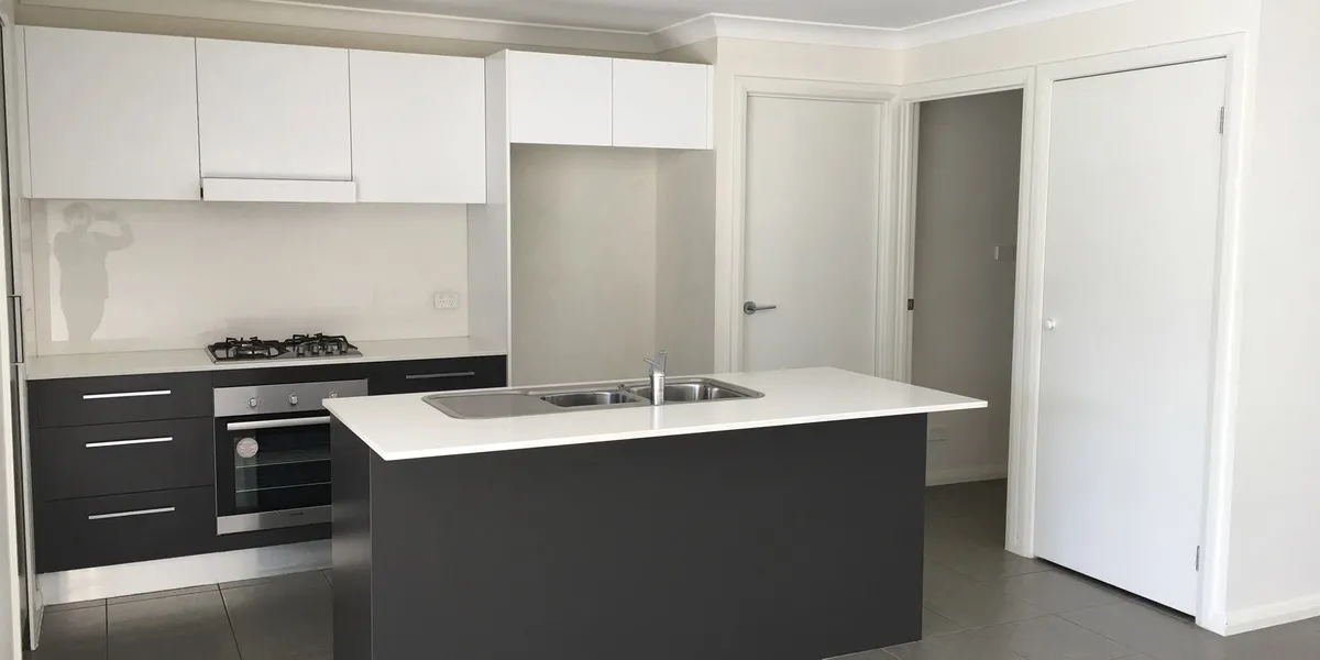 A white kitchen with a dark island bench, cleaned and empty