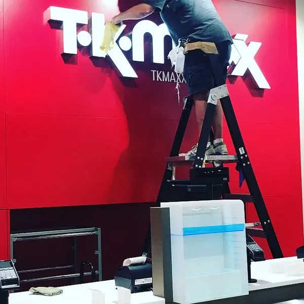 A cleaner on a ladder wiping the TK Maxx sign in a new store