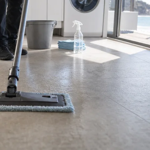 A flat mop drawn across pale tiles in a laundry, the wet stripe behind it