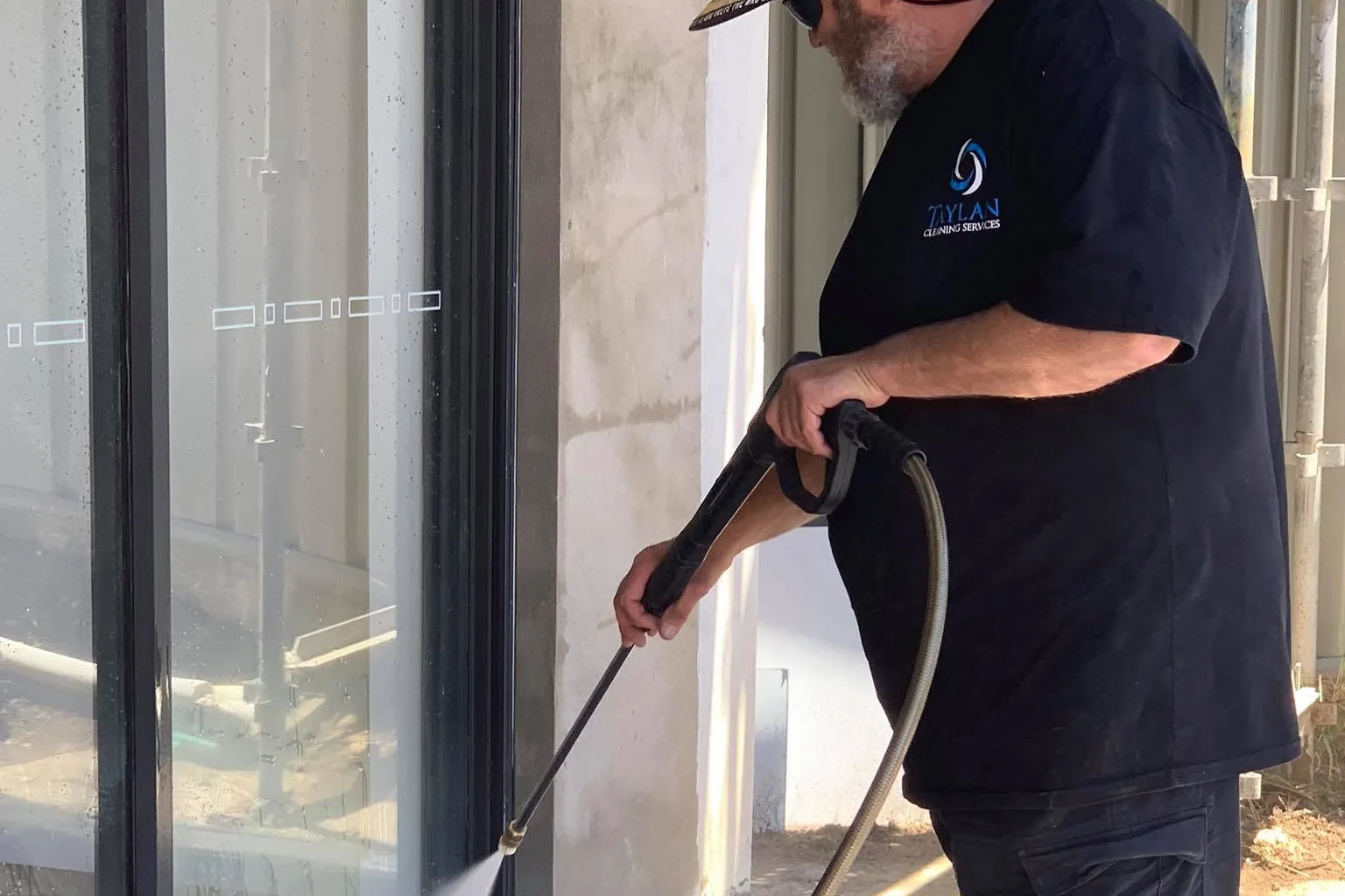 A Taylan cleaner pressure washing a concrete slab beside a glass door
